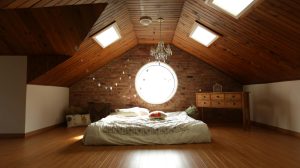 A warm and inviting attic bedroom featuring a unique brick wall and wooden ceiling design. Une chambre mansardée chaleureuse et accueillante avec un mur en briques unique et un design de plafond en bois.