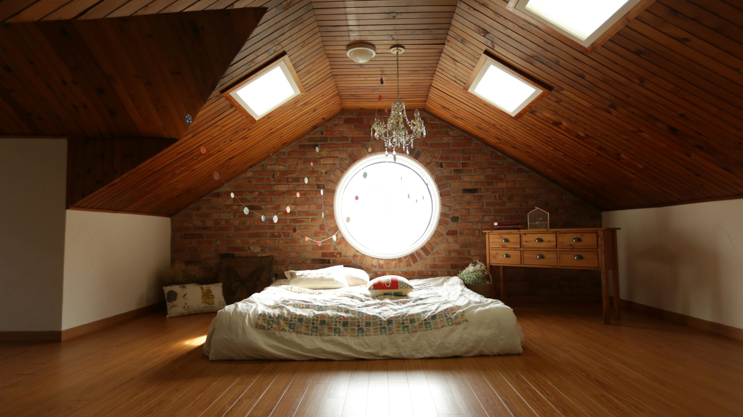 A warm and inviting attic bedroom featuring a unique brick wall and wooden ceiling design. Une chambre mansardée chaleureuse et accueillante avec un mur en briques unique et un design de plafond en bois.