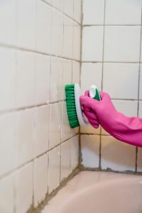 Une personne nettoie des carreaux de salle de bain en portant un gant rose, mettant l'accent sur la propreté.