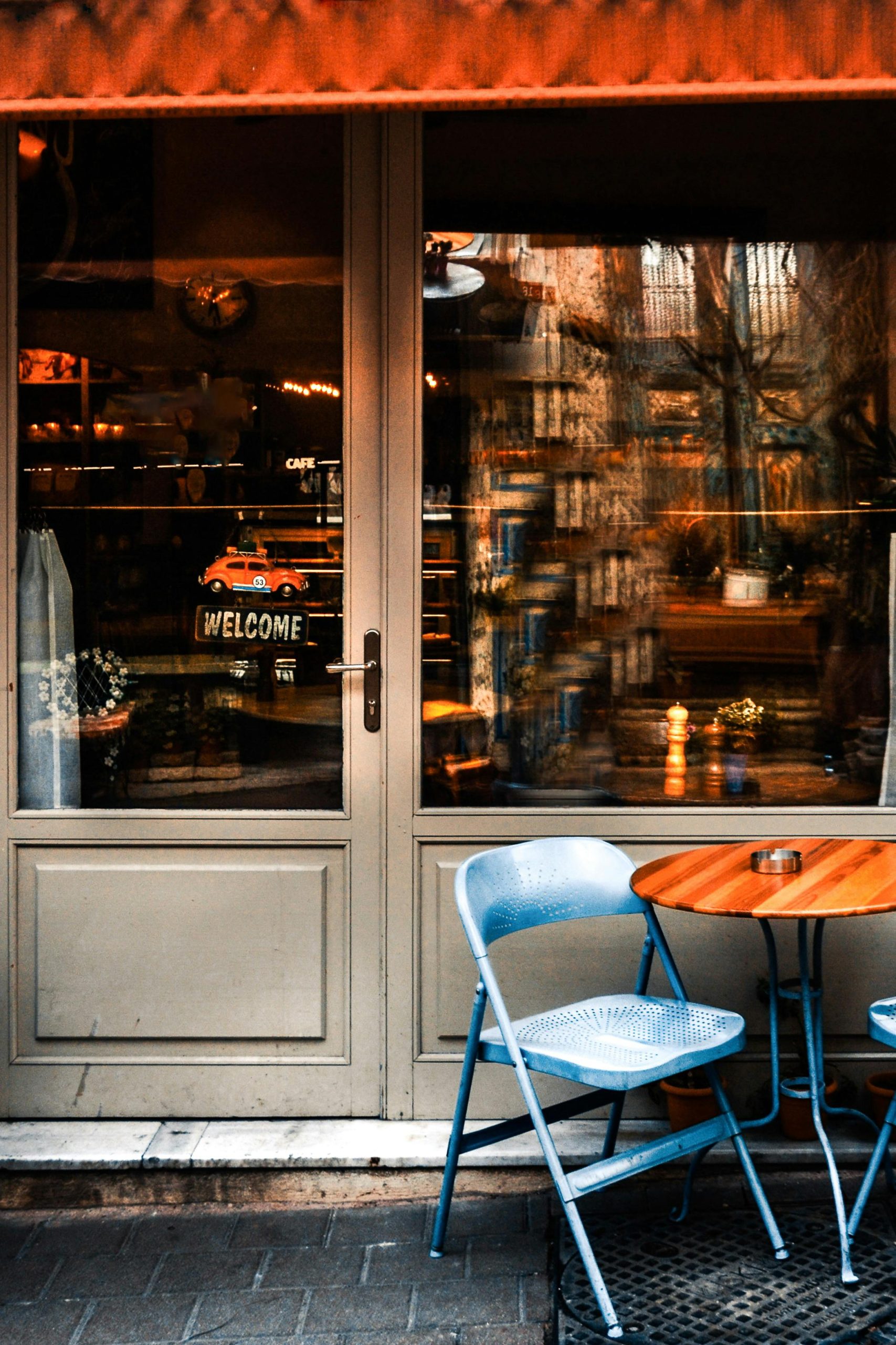 A charming urban café entrance with a blue chair and table, inviting with a warm ambiance. Une entrée de café urbain charmante avec une chaise et une table bleues, invitante avec une ambiance chaleureuse.