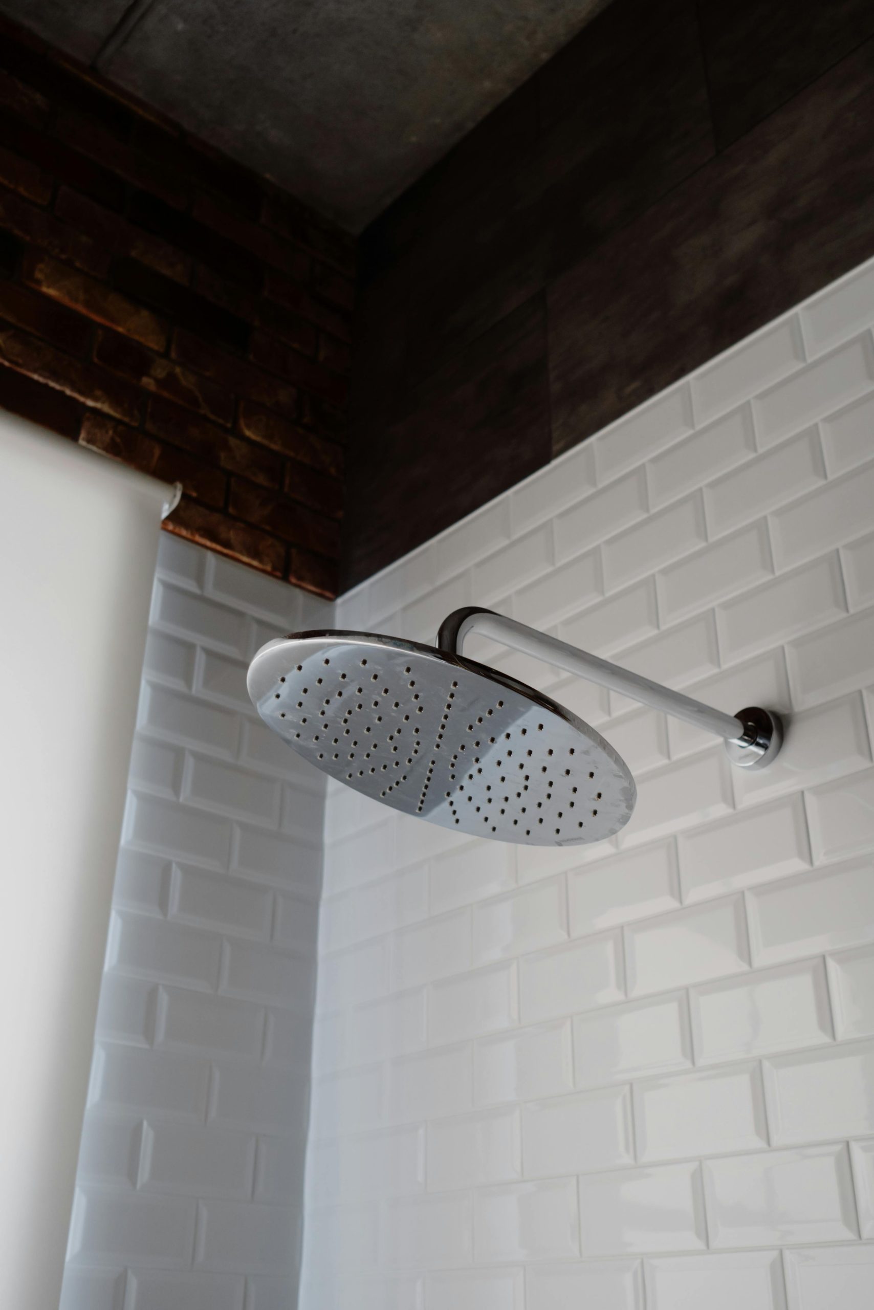 Tête de douche en acier inoxydable élégante contre une salle de bain élégante avec carrelage blanc et un mur d'accent en briques.