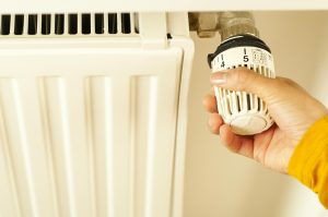 Close-up of hand adjusting radiator thermostat to control home heating temperature. Gros plan sur une main réglant le thermostat du radiateur pour contrôler la température de chauffage de la maison.