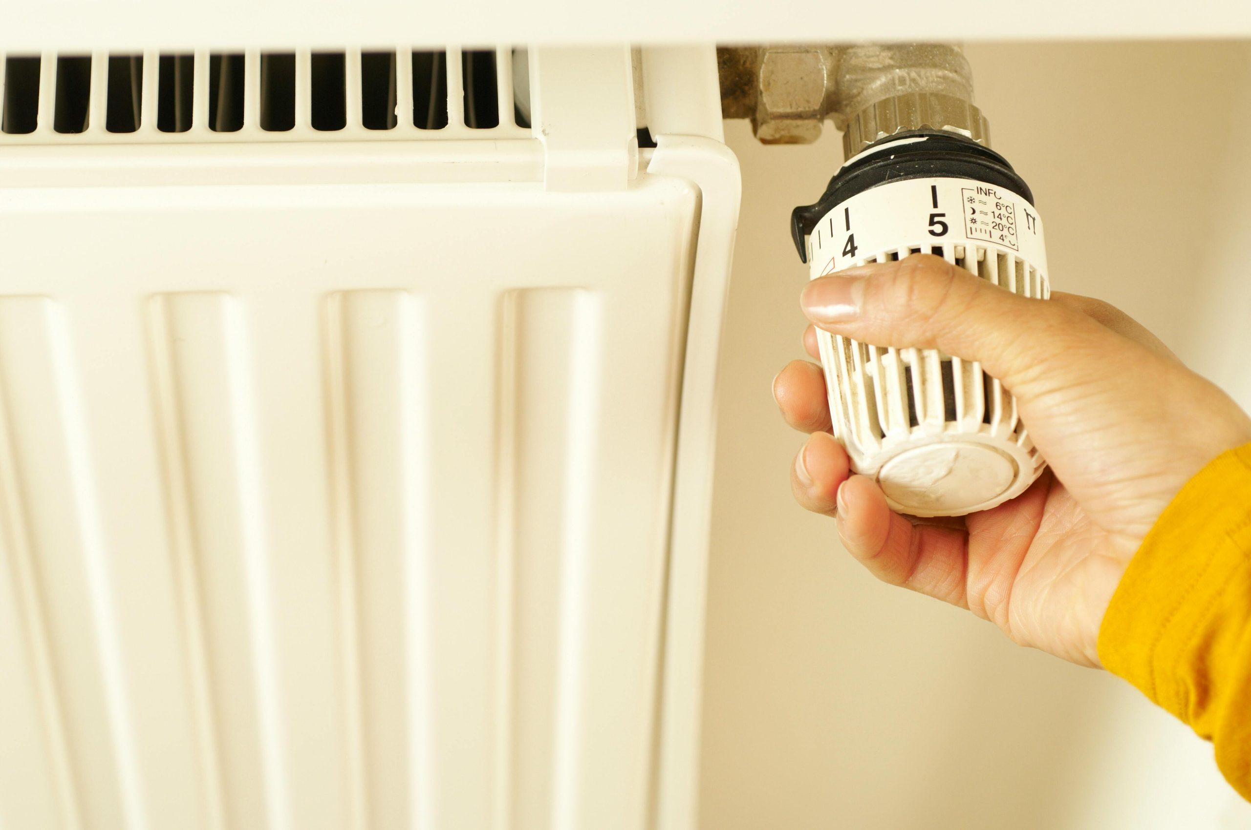 Close-up of hand adjusting radiator thermostat to control home heating temperature. Gros plan sur une main réglant le thermostat du radiateur pour contrôler la température de chauffage de la maison.