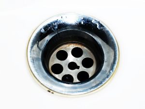 Detailed image of a chrome sink drain showcasing water droplets and a metallic finish. Image détaillée d'une bonde d'évier chromée mettant en avant des gouttes d'eau et une finition métallique.