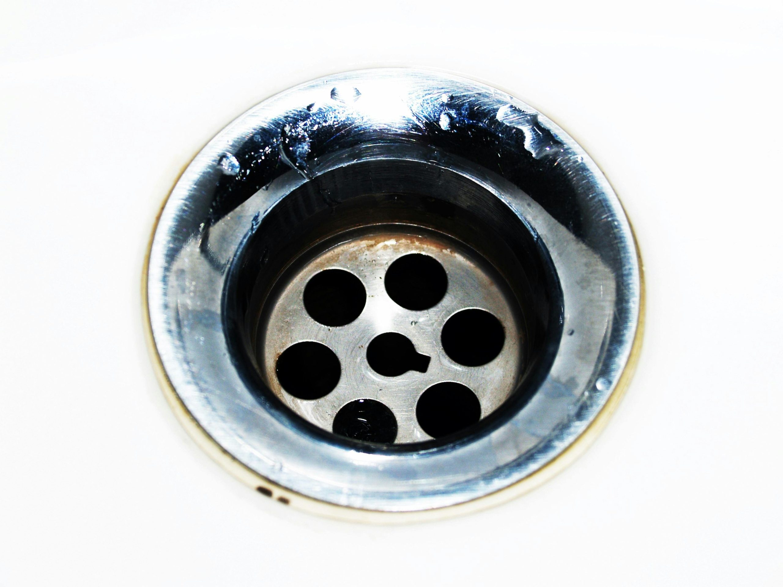 Detailed image of a chrome sink drain showcasing water droplets and a metallic finish. Image détaillée d'une bonde d'évier chromée mettant en avant des gouttes d'eau et une finition métallique.