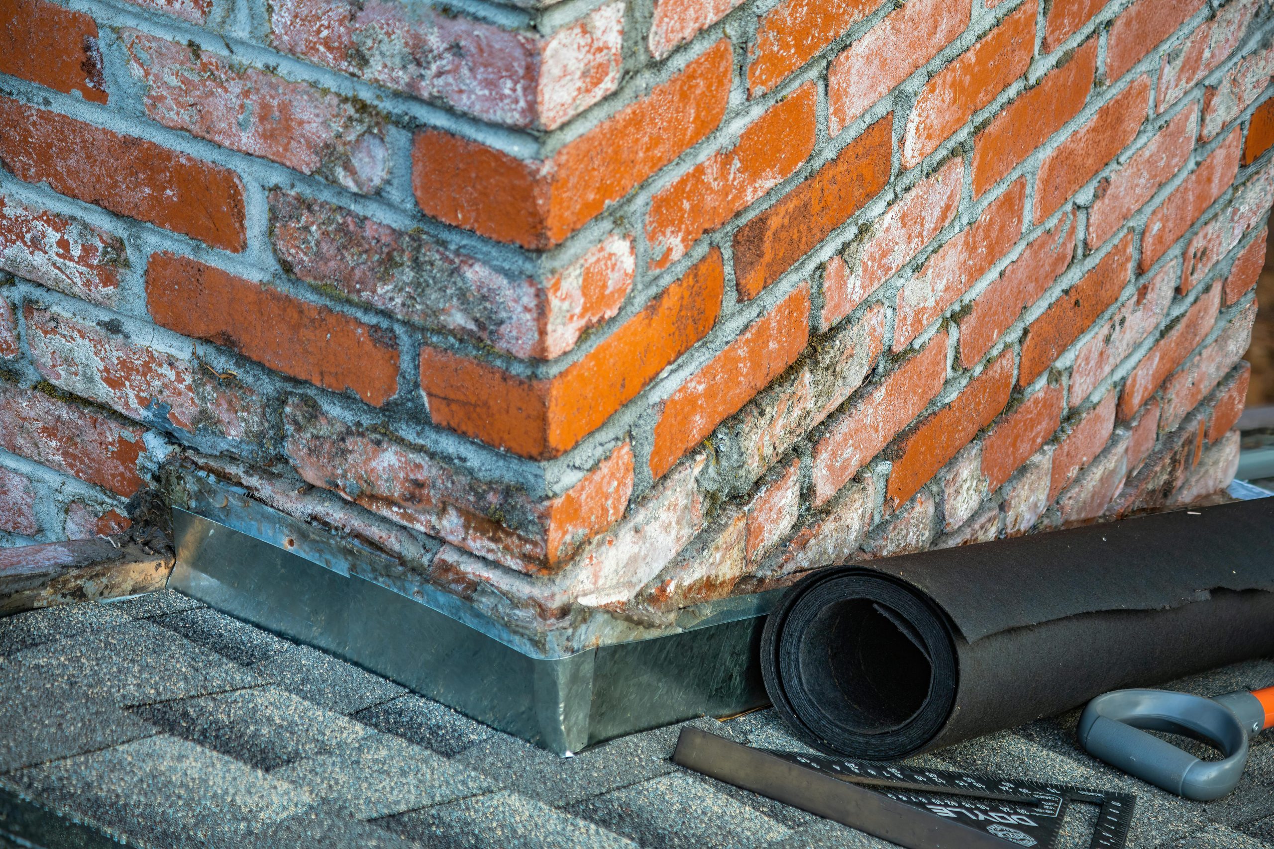 Detailed view of a brick chimney featuring construction tools and materials for repair. Vue détaillée d'une cheminée en briques présentant des outils de construction et des matériaux de réparation.