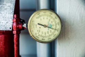 Detailed view of a pressure gauge attached to a red industrial pipe, measuring PSI and kPa. Vue détaillée d'un manomètre attaché à un tuyau industriel rouge, mesurant PSI et kPa.