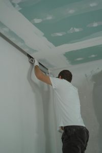 A man works meticulously on drywall installation during a house renovation. Un homme travaille avec soin à l'installation de cloisons sèches lors d'une rénovation domiciliaire.