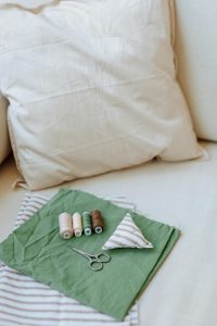 A detailed view of sewing supplies including fabric, threads, and scissors on a cushion. Une vue détaillée des fournitures de couture comprenant du tissu, des fils et des ciseaux sur un coussin.
