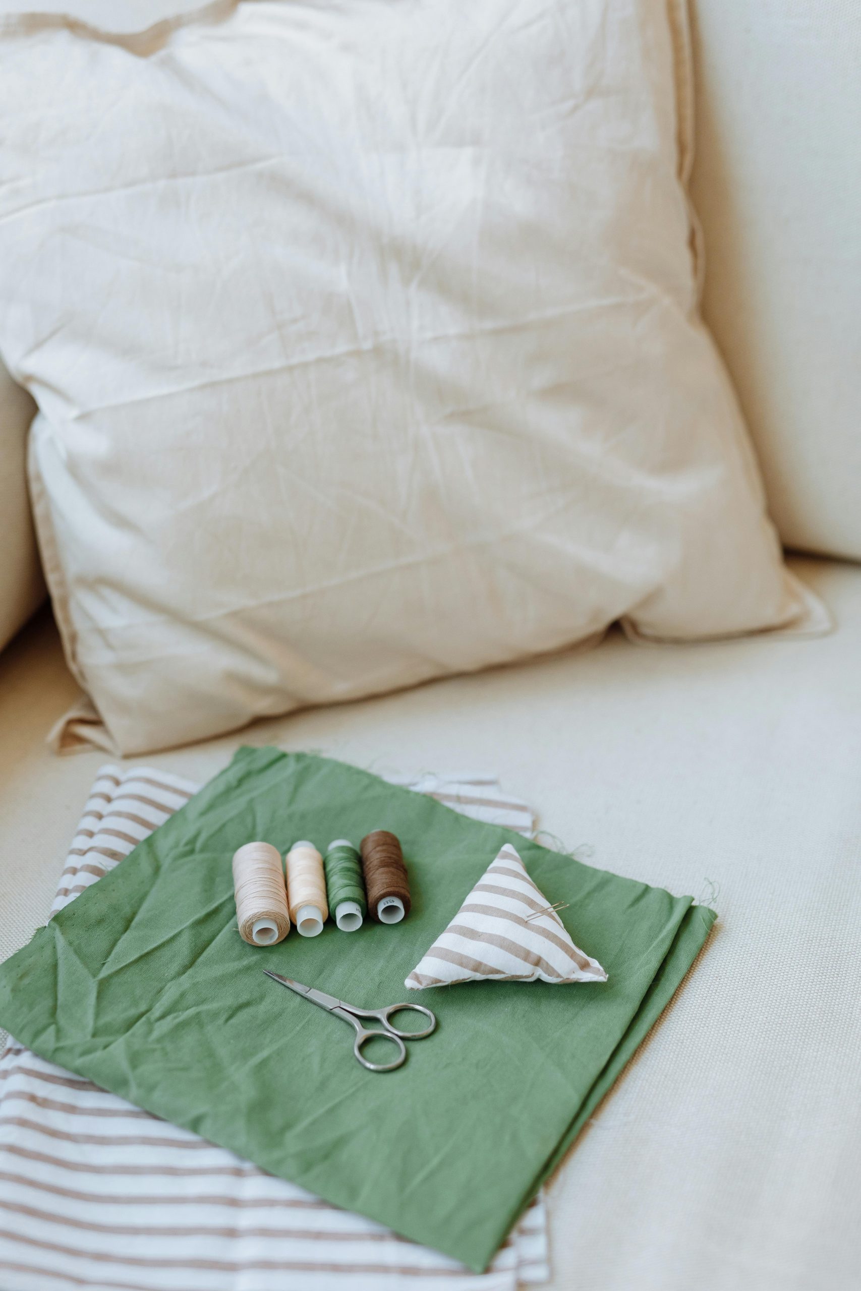 A detailed view of sewing supplies including fabric, threads, and scissors on a cushion. Une vue détaillée des fournitures de couture comprenant du tissu, des fils et des ciseaux sur un coussin.