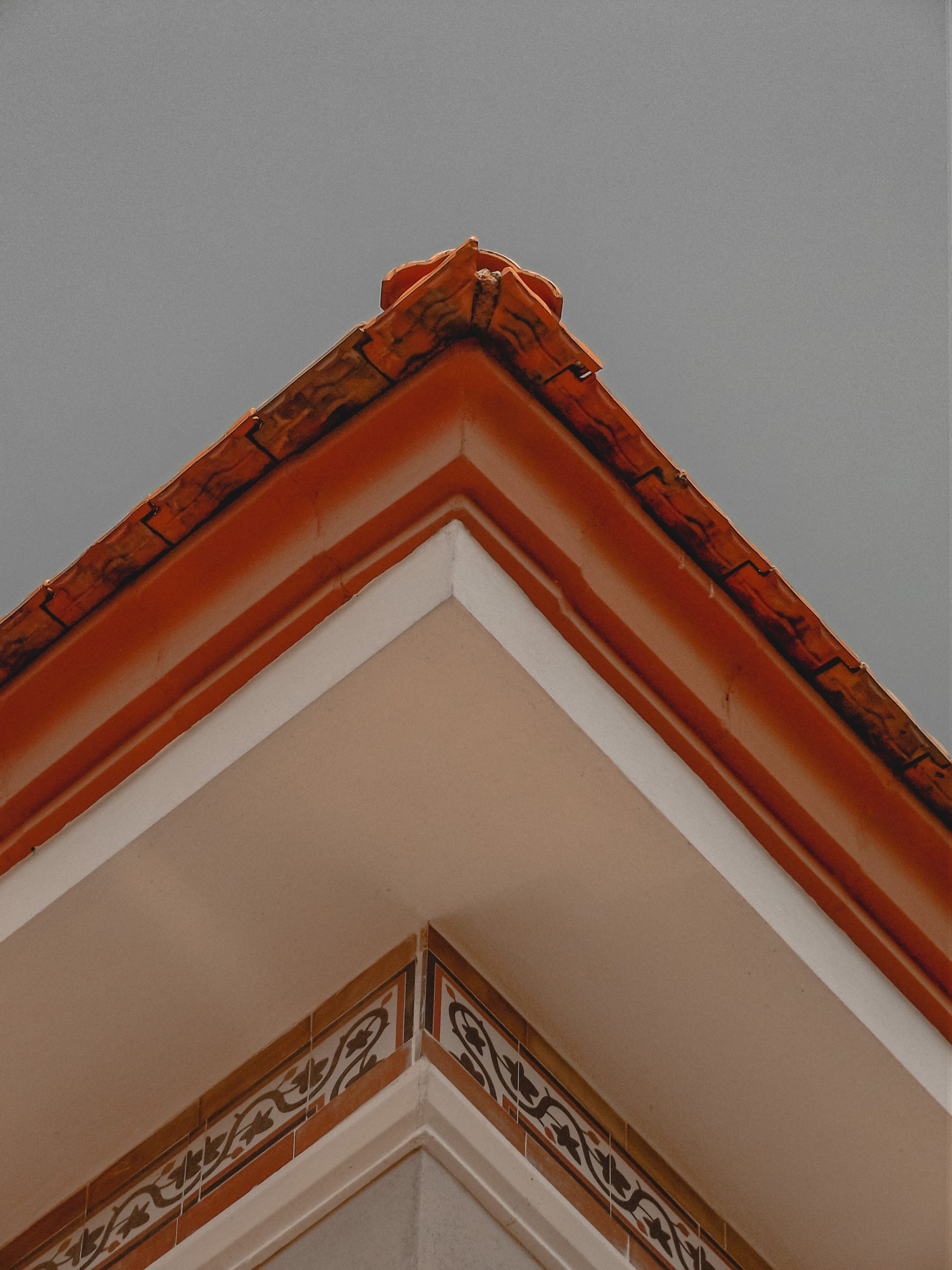 A distinct perspective of a decorative tiled rooftop corner with intricate designs against a gray sky. Une perspective distincte d'un coin de toit carrelé décoratif avec des motifs complexes sur un ciel gris.