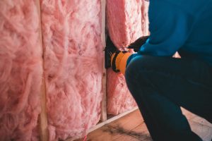 Crop unrecognizable worker in gloves sitting on haunches and insulating with pink stone wool Travailleur méconnaissable en gants accroupi et isolant avec de la laine de pierre rose