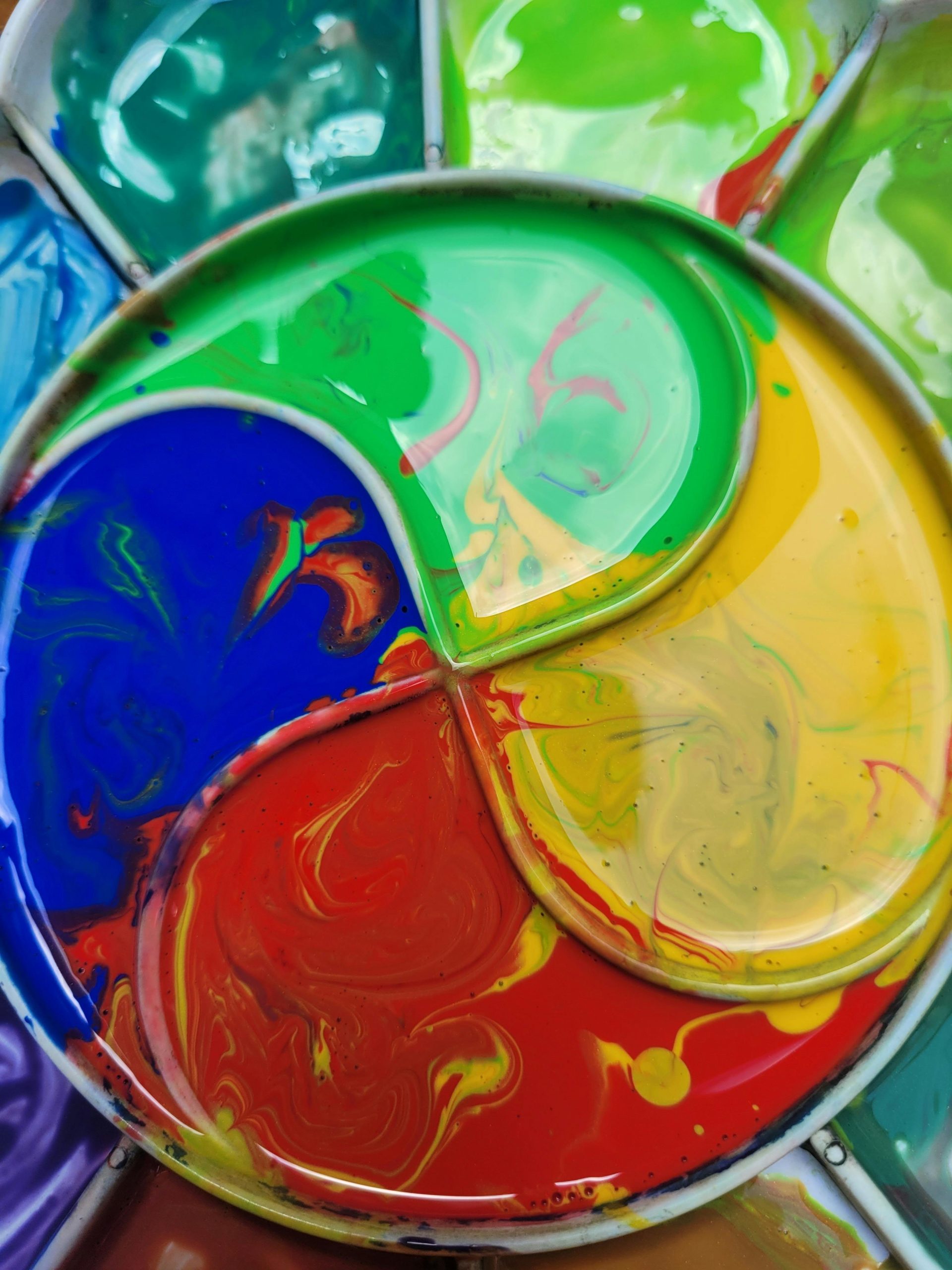 Close-up of vibrant paint swirls in a circular art palette, showcasing colorful patterns. Gros plan sur des tourbillons de peinture vibrante dans une palette d'art circulaire, mettant en évidence des motifs colorés.