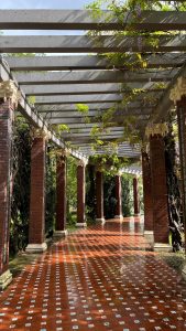 A scenic outdoor colonnade with vibrant brick and lush foliage on a sunny day. Une colonnade extérieure pittoresque avec des briques vibrantes et un feuillage luxuriant par une journée ensoleillée.