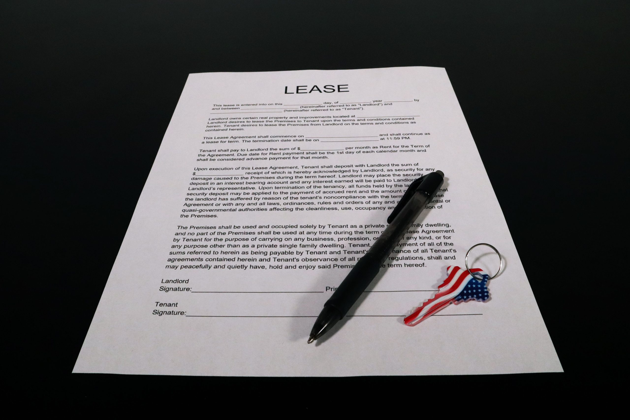 Lease agreement document with pen and American flag keychain on a black table. Document d'accord de location avec stylo et porte-clés drapeau américain sur une table noire.