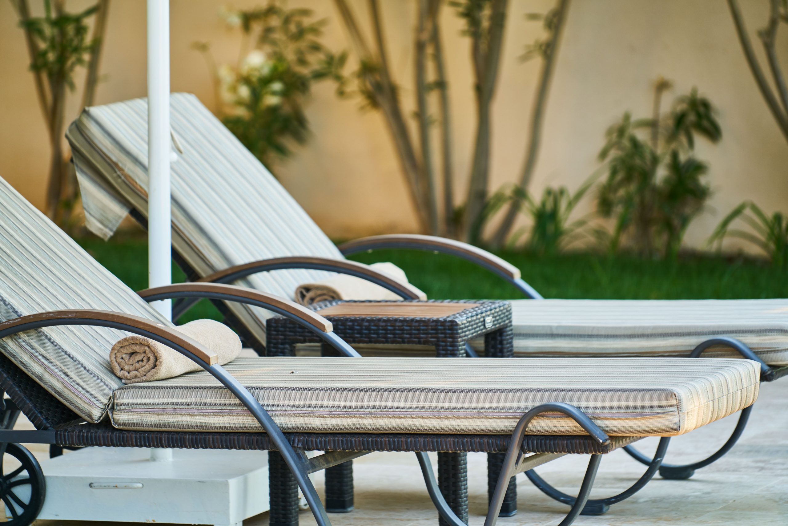 Elegant wooden sun loungers lined up poolside at a tropical resort, perfect for relaxation. Des transats en bois élégants alignés au bord de la piscine dans une station balnéaire tropicale, parfaits pour la détente.