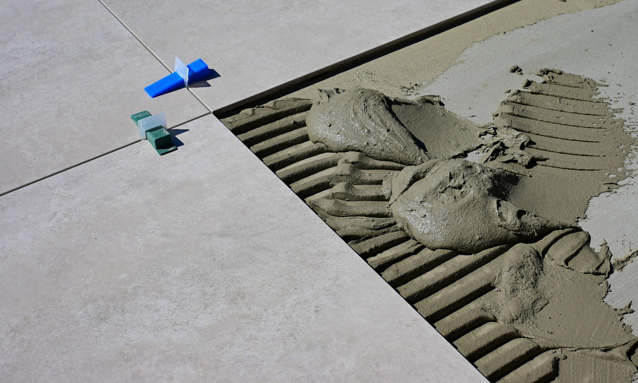 Close-up of wet cement and tile spacers during floor tile installation. Gros plan sur du ciment humide et des espaceurs de carrelage lors de l'installation de carreaux de sol.